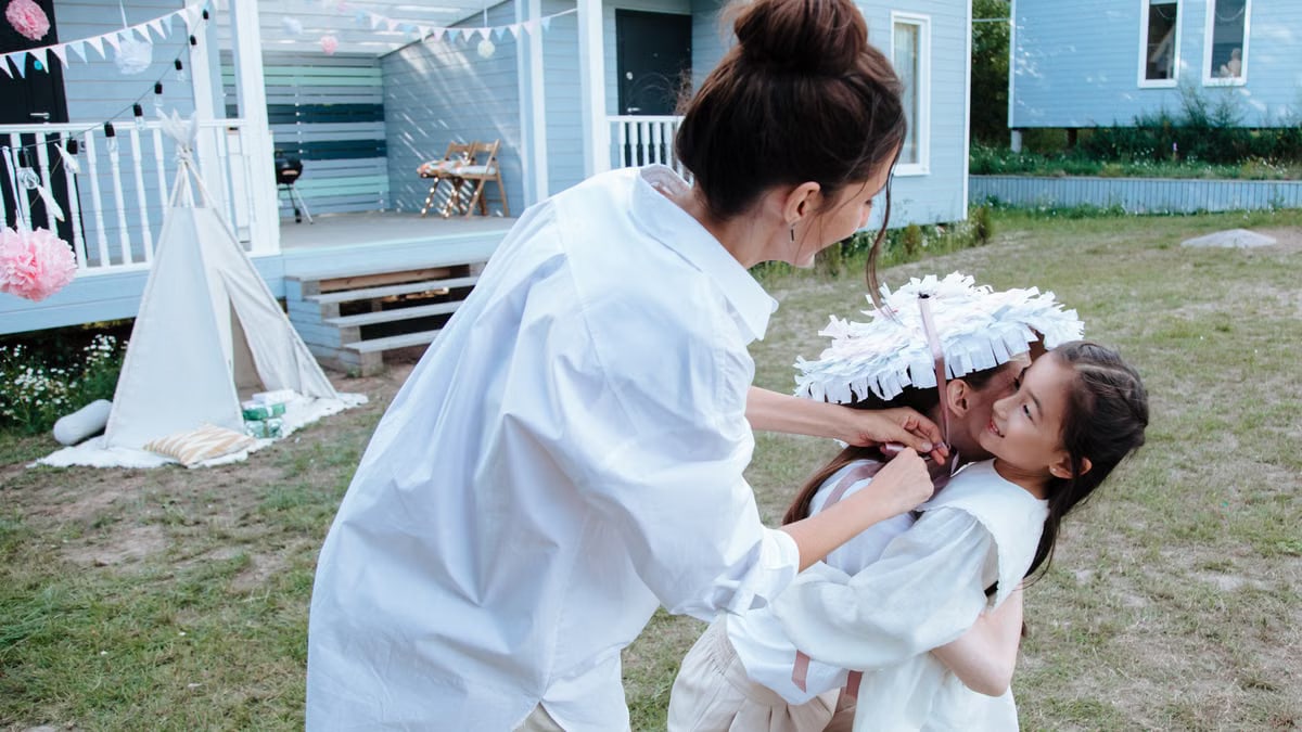 Mother and daughter enjoying a playful moment outdoors in a festive backyard setting.